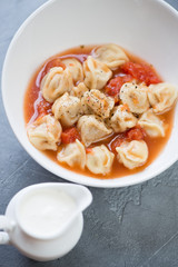 Soup with meat dumplings pelmeni served in a white bowl, close-up, elevated view