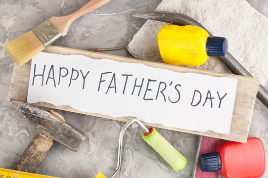 Handwritten inscription happy fathers day on torn white paper near scattered tools on old gray concrete