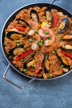 Paella with seafood in a serving pan, elevated view over blue stone surface, vertical shot