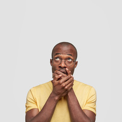 I will say nothing nothing! Emotive dark skinned middle aged male close mouth and looks in bewilderment upwards, tries to be mute, isolated over white background. People and puzzlement concept