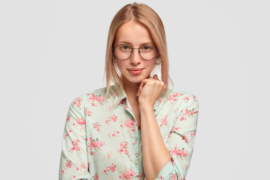 Adorable European female arhitect looks delightfully at camera, wears glasses and spectacles, listens attentively client, takes into account details of designing, isolated over white background
