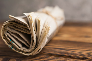 Roll of related old newspapers on old brown wooden table on background of concrete wall with copy space for your text