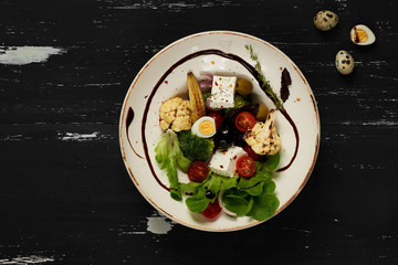 Tasty vegetarian salad made of quail eggs, lettuce, Feta cheese, broccoli, cauliflower, olives and baby corn on plate standing on blue old wooden table. Healthy dietary meal, wholesome dish. Top view.