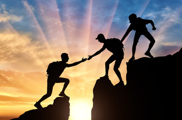 Silhouette of two climbers in the mountains help another climber to overcome the obstacle