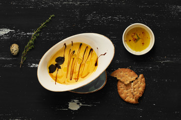 Creamy vegetable soup in oval plate, cracker, thyme and quail egg on blue aged wooden surface. Delicious gourmet restaurant dish, tasty vegetarian daily meal, appetizing veggie food. Top view.