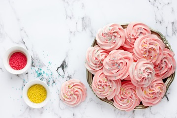 Homemade marshmallow, fluffy dessert zephyr, pink swirl meringue with colorful sugar sprinkles in bowl on a marble background top view