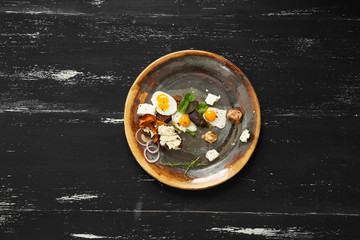 Bruschetta with cream cheese, fried eggs, mushrooms and salad leaves lying on plate standing on blue aged wooden surface with quail eggs and bread sticks scattered around. Tasty daily meal. Top view.