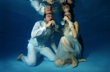Bride and groom drink red wine underwater in the pool. Underwater wedding