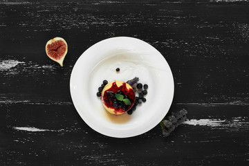 Delicious cake served with blueberries, jam and mint leaves on round plate, fig and cornflowers lying on blue aged wooden surface. Tasty gourmet berry dessert, appetizing sweet meal. Top view.