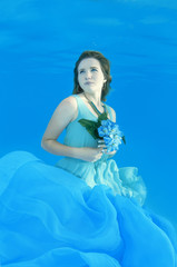 Fototapeta na wymiar Young beautiful woman in a pale blue dress with a bouquet of flowers posing under water (for the calendar, spring, March)