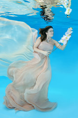 Fototapeta na wymiar Young beautiful woman in a beige dress and a flower in hands posing under water (for the calendar, spring, April)