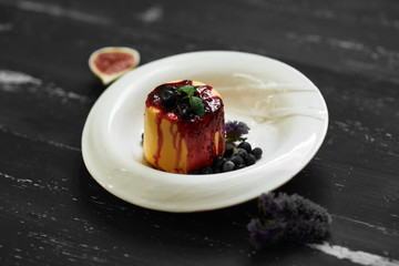 Delicious cake served with blueberries, jam and mint leaves on round plate, fig and cornflowers lying on blue aged wooden surface. Tasty gourmet berry dessert, appetizing sweet meal. Top view.