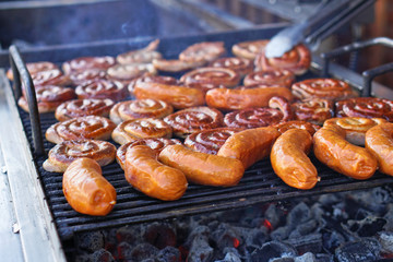 Grilled sausage on a grill with a delicious crust on the background of vegetables. Summer holidays and food in nature. Stock Photo