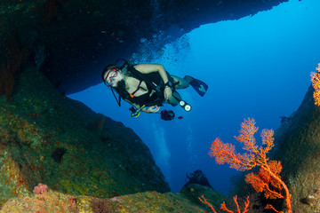 Naklejka na ściany i meble Female SCUBA diver swimming through an underwater tunnel on a tropical coral reef