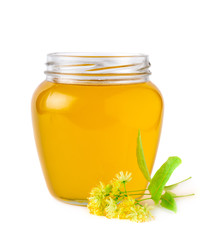 Glass jar of fresh linden honey with flowers of linden on white.