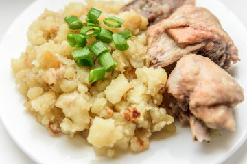 Stewed potatoes with chicken and green onions on white plate.