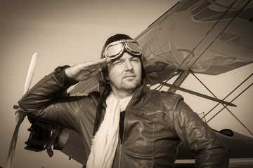 
Portrait of a vintage pilot with leather cap, scarf and aviator glasses salutes in front of a...
