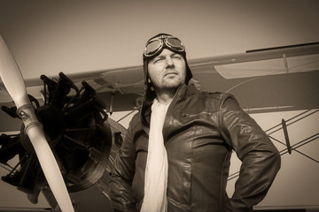 Portrait of a vintage pilot with leather cap, scarf and aviator glasses in front of a historic...