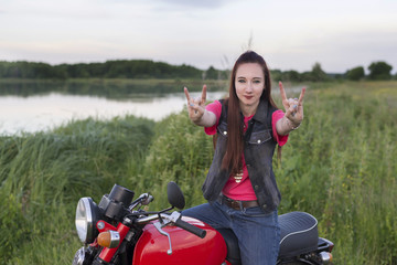 Fototapeta na wymiar A girl on a vintage motorcycle shows a goat sign outdoors