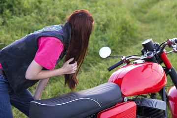 Fototapeta na wymiar A girl stands near vintage motorcycle and looks in the mirror outdoors