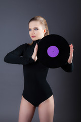 A beautiful girl is holding a vinyl disk. Studio photography on a gray background