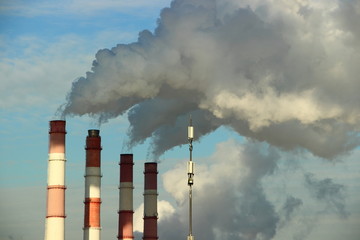 Industry, industry and ecology - dirty grey smoke from the red-white pipes of the plant (chemical plant power plant), thermal power plant against the blue clear sky