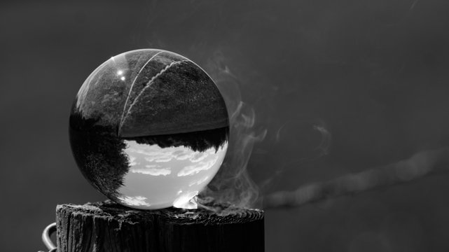 Photo Spere crystal ball reflecting and magnifying sun beams to burn fence post with countryside screne reflected upside down in ball