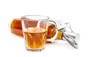 Bottle and glass with alcohol drink and handcuffs on white. Alcohol dependence concept.