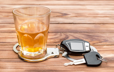 Glass with alcoholic drink, handcuffs and car key on wooden table.