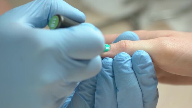 Nail master apply colorful gel poplish. Manicure master in rubber gloves apply turquoise gel polish shellac on a woman hand finger nail close up.