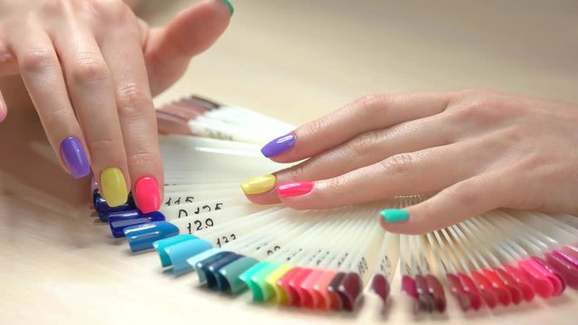Young woman hands and nails polish palette. Female hand with beautiful summer manicure choosing nail varnish color on table in nail salon.