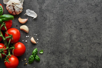 Food background. Flat lay of fresh tomatoes with basil, garlic and seasalt on black stone...