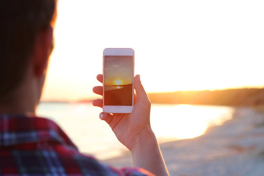 guy makes a photo on a modern smartphone on a sunset background by the sea