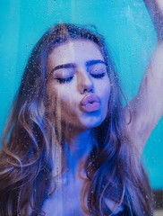 spa and beauty. spa treatment of young woman with long curly hair holding window glass with water drops.