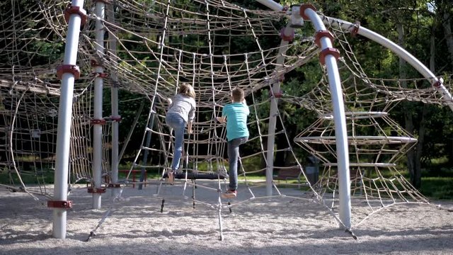 Happy two children in adventure park. Cute teen boy and girl having fun and climbing on a rope at playground outdoors.