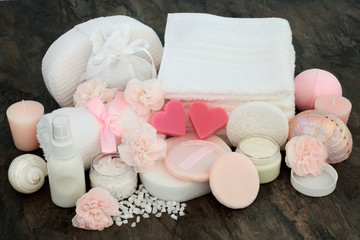 Spa beauty treatment products including pink moisturising cream, ex foliating salt, heart shaped soap, flowers, sponges,  powder puffs,  body lotion and decorative seashells on marble background.