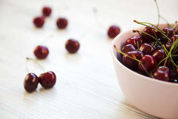 Fresh sweet cherries in a bowl on white wooden background. Side view.