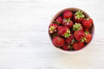Fresh strawberries in a pink ceramic bowl on white wooden background, top view. From above. Copy space.