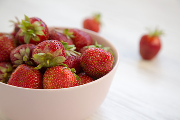 Fresh strawberries in a pink ceramic bowl on white wooden table, side view. Close-up.