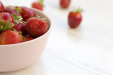 Fresh ripe strawberries in a pink bowl on white wooden table, side view. Close-up.