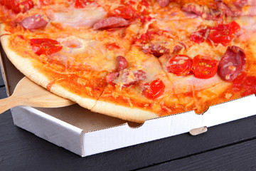 Pizza on a black wooden background with wooden cutlery, Italian pizza with tomatoes, bacon, sausages and cheese, fast food, festive food on a dark background, copy space, Italian cuisine