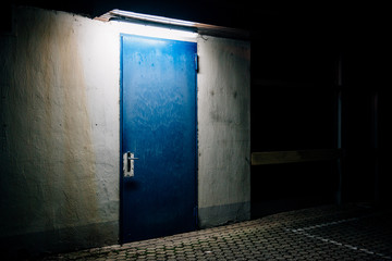 One blue door in the darkness illuminated from the above in empty city