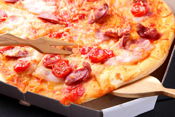 Pizza on a black wooden background with wooden cutlery, Italian pizza with tomatoes, bacon, sausages and cheese, fast food, festive food on a dark background, copy space, Italian cuisine