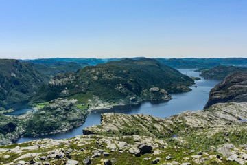 Fototapeta premium View at lysefjorden and the Norwegian landscape from above Preikestolen/Pulpit Rock in Norway with a clear blue sky. Hiking further up than Preikestolen/Pulpit Rock gave us this reward. 
