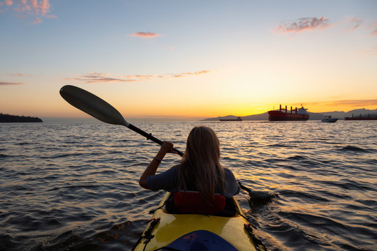 Woman on a kayak is paddeling in the ocean during a vibrant sunset. Taken in Vancouver, British Columbia, Canada. Concept: adventure, holiday, lifestyle, sport, recreation, activity, vacation