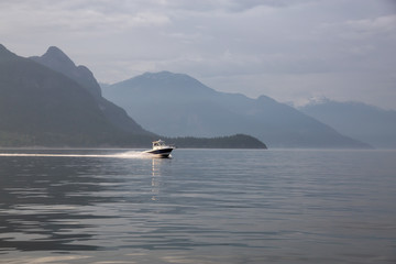 Fototapeta na wymiar Speed boat in the ocean surrounded by the Canadian Mountain Landscape. Taken in Howe Sound, North of Vancouver, British Columbia, Canada.