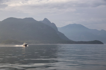 Speed boat in the ocean surrounded by the Canadian Mountain Landscape. Taken in Howe Sound, North of Vancouver, British Columbia, Canada.