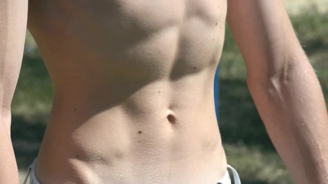 Young sexy guy shows his strong abdominal muscles during workout exercise in a Park