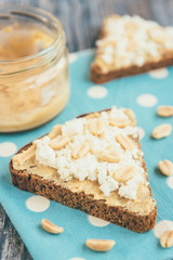 Bread with peanut butter, cottage cheese and peanut on wooden background. Healthy breakfast or snack.