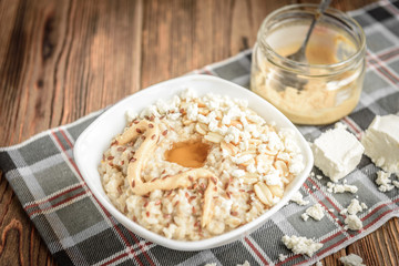 Homemade oatmeal with honey, peanut butter, peanut, flax seeds and cottage cheese on wooden background. Healthy breakfast.